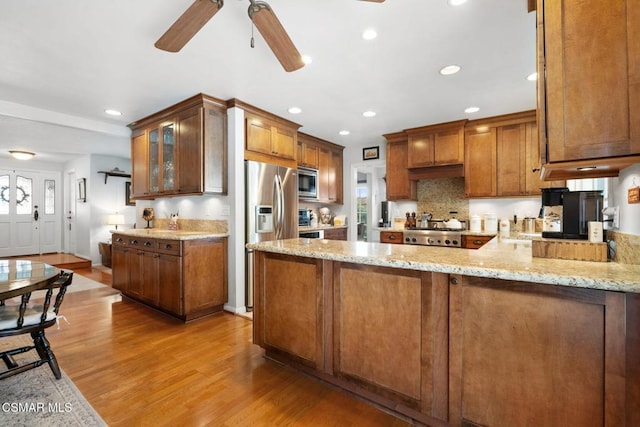 kitchen with light hardwood / wood-style flooring, appliances with stainless steel finishes, kitchen peninsula, a wealth of natural light, and light stone countertops