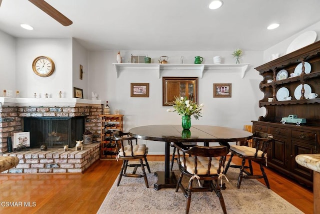 dining space with a fireplace, wood-type flooring, and ceiling fan