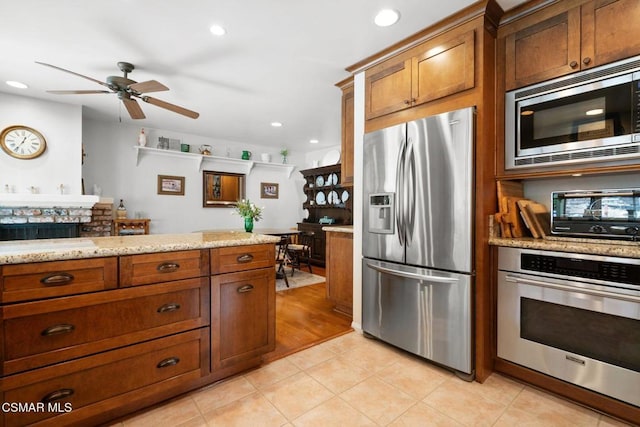 kitchen with appliances with stainless steel finishes, light tile patterned floors, light stone counters, and ceiling fan