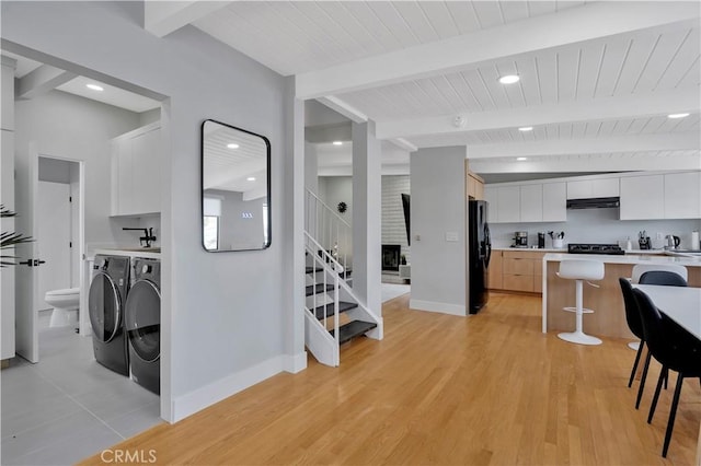 kitchen with white cabinetry, black refrigerator, beam ceiling, ventilation hood, and washing machine and clothes dryer