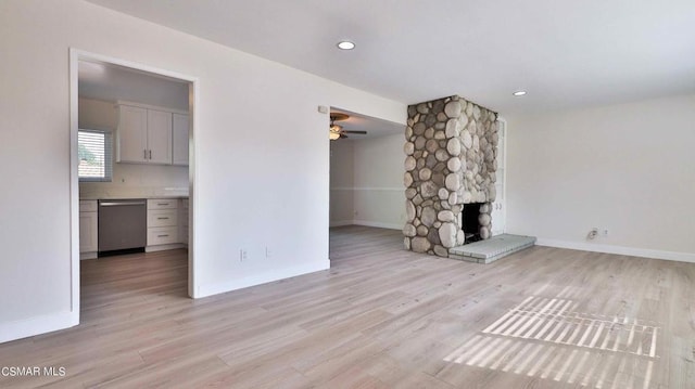 unfurnished living room featuring ceiling fan, a stone fireplace, and light hardwood / wood-style floors