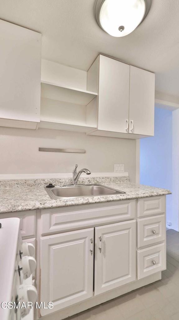 kitchen featuring white cabinetry, light stone countertops, sink, and light tile patterned flooring