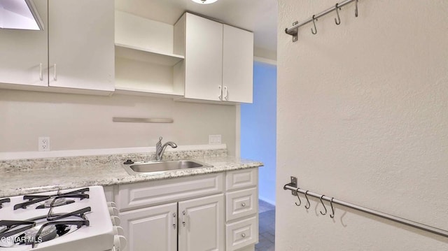 kitchen featuring gas range, light stone countertops, sink, and white cabinets