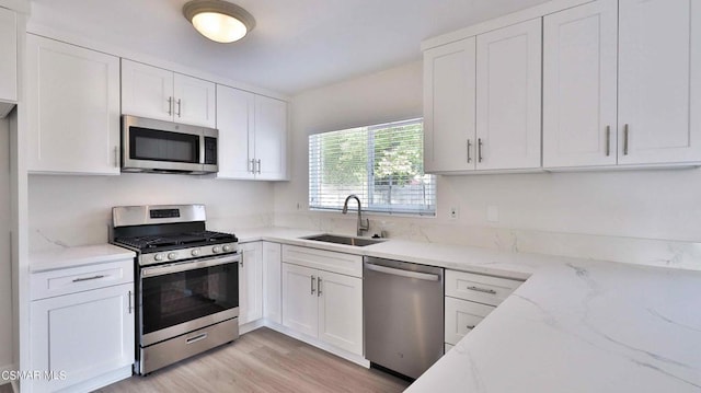 kitchen with appliances with stainless steel finishes, light stone countertops, sink, and white cabinets