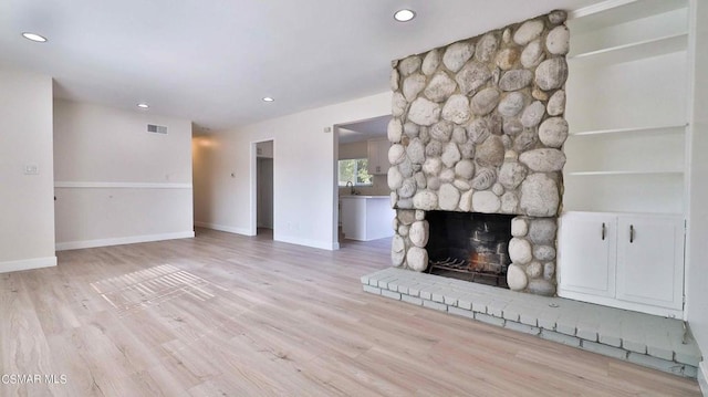 unfurnished living room featuring a stone fireplace and light hardwood / wood-style floors