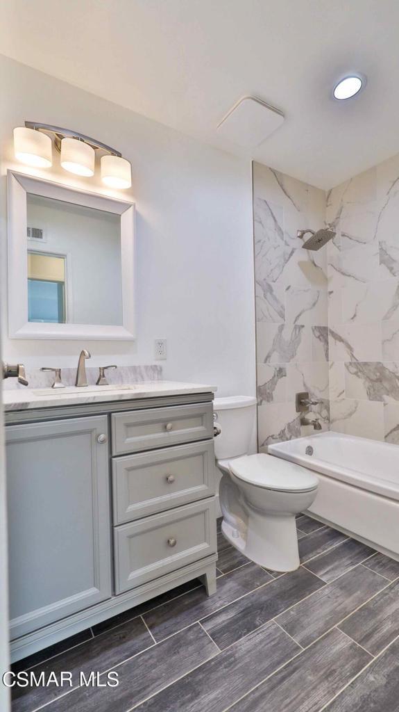 full bathroom featuring tiled shower / bath, vanity, and toilet