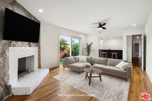 living room with ceiling fan, a brick fireplace, and light wood-type flooring