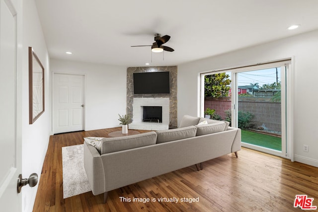 living room featuring ceiling fan, a large fireplace, and wood-type flooring