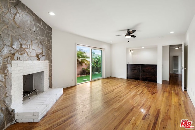 unfurnished living room with wood-type flooring, a large fireplace, and ceiling fan