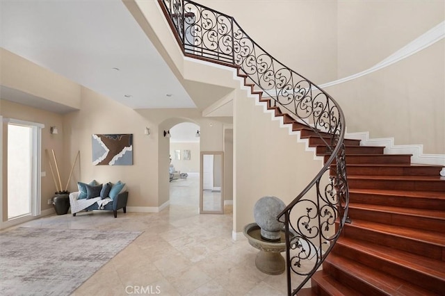 stairs featuring a high ceiling, baseboards, and arched walkways
