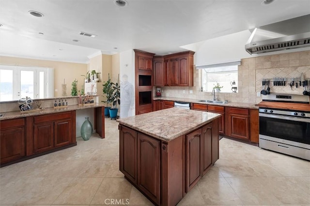 kitchen featuring wall chimney range hood, a sink, visible vents, dishwashing machine, and stainless steel range oven