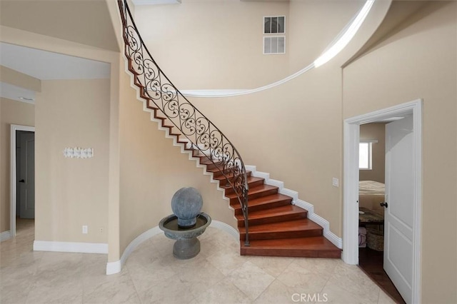 staircase with baseboards, visible vents, and a high ceiling