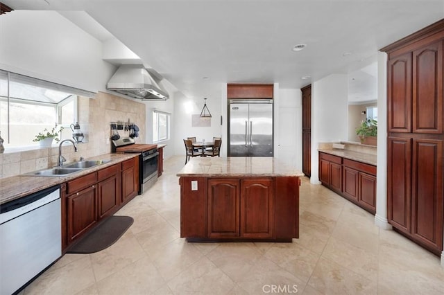 kitchen featuring sink, a center island, stainless steel appliances, light stone countertops, and wall chimney range hood