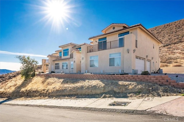 view of front of house featuring stucco siding, a tiled roof, a balcony, and an attached garage