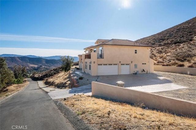 view of home's exterior with driveway, fence, a mountain view, an attached garage, and stucco siding