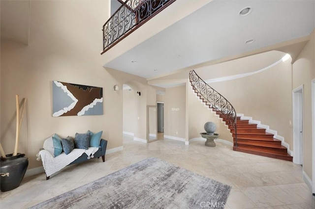 entrance foyer featuring arched walkways, stairs, baseboards, a towering ceiling, and tile patterned flooring