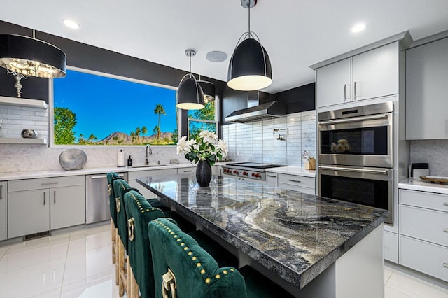 kitchen featuring wall chimney exhaust hood, sink, appliances with stainless steel finishes, gray cabinets, and a kitchen island