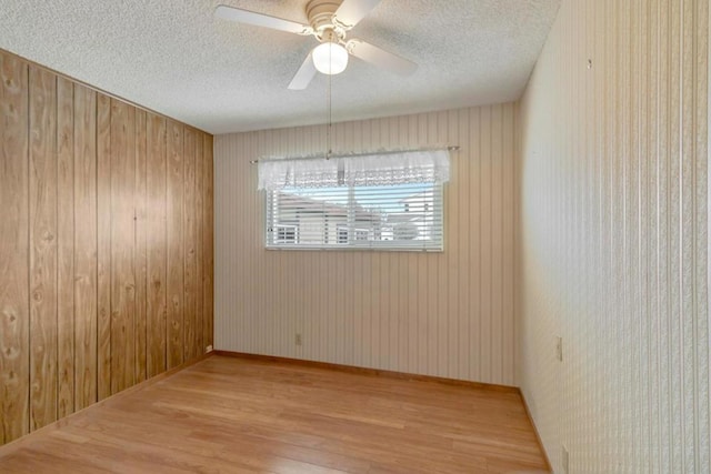 unfurnished room with a textured ceiling, light hardwood / wood-style flooring, ceiling fan, and wood walls