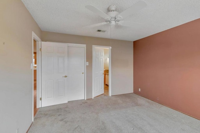 unfurnished bedroom featuring ceiling fan, light colored carpet, a closet, and a textured ceiling