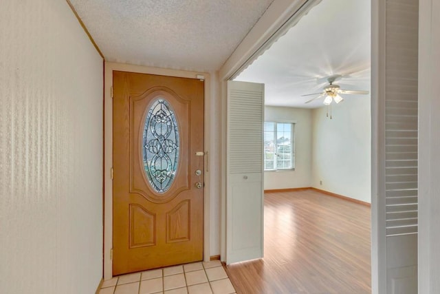 foyer with ceiling fan, a textured ceiling, and light tile patterned floors