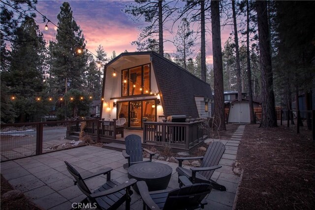 back house at dusk with a wooden deck, a patio, and a shed