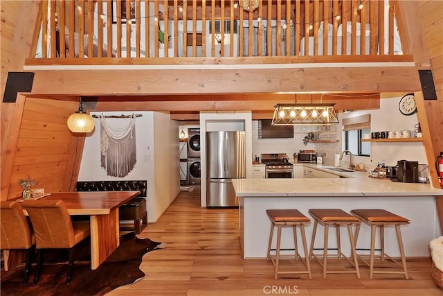 kitchen featuring appliances with stainless steel finishes, decorative light fixtures, sink, stacked washer / drying machine, and kitchen peninsula