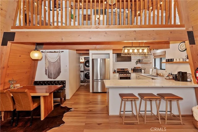 kitchen featuring stacked washer and clothes dryer, appliances with stainless steel finishes, hanging light fixtures, a peninsula, and a sink