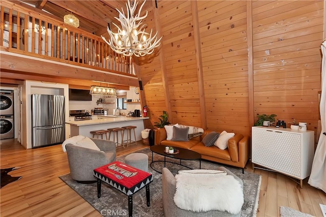 living room with stacked washing maching and dryer, a high ceiling, a notable chandelier, wooden ceiling, and beam ceiling