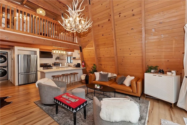 living area with an inviting chandelier, wood walls, stacked washing maching and dryer, light wood-type flooring, and wooden ceiling