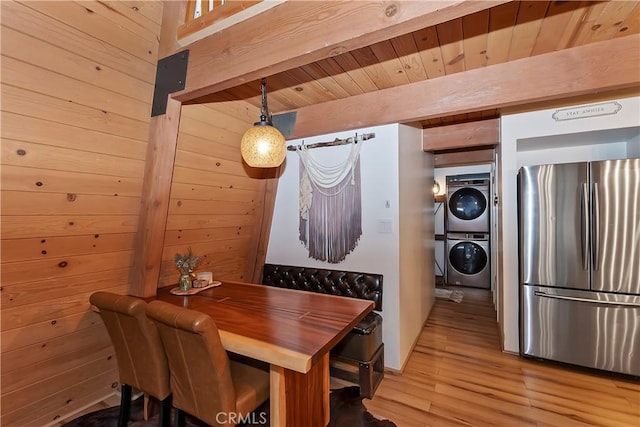 dining room featuring wooden ceiling, stacked washer and clothes dryer, light wood-type flooring, and wood walls