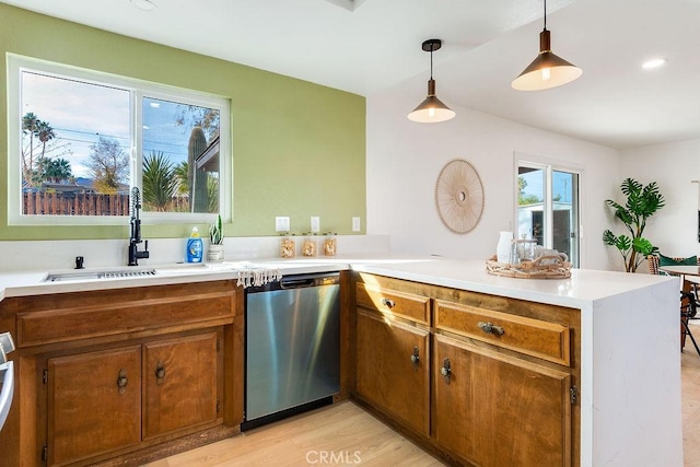 kitchen featuring sink, light hardwood / wood-style flooring, stainless steel dishwasher, kitchen peninsula, and pendant lighting