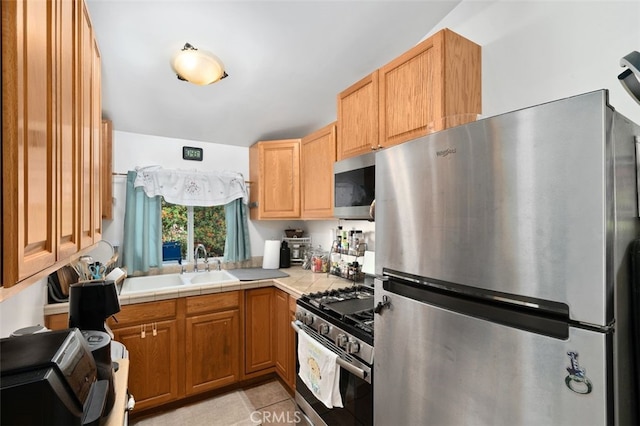 kitchen with light tile patterned flooring, stainless steel appliances, tile counters, and sink