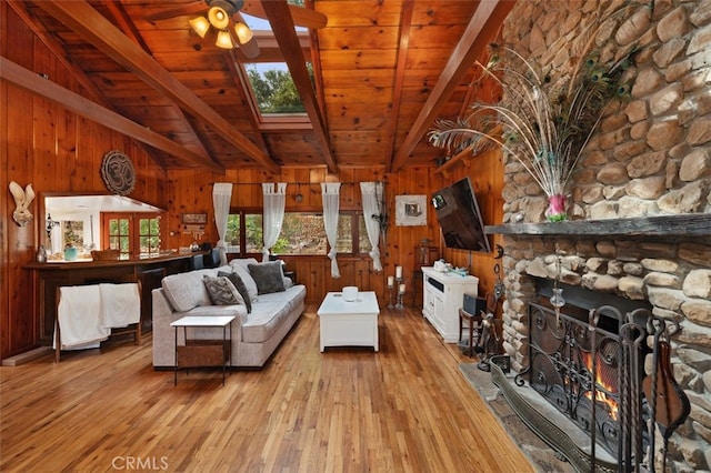 unfurnished living room featuring a stone fireplace, wooden ceiling, light wood-type flooring, wooden walls, and vaulted ceiling with skylight