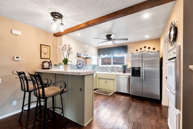 kitchen featuring appliances with stainless steel finishes, tasteful backsplash, green cabinetry, a kitchen bar, and kitchen peninsula