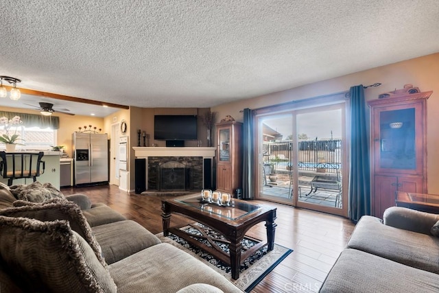 living room featuring hardwood / wood-style flooring, ceiling fan, a textured ceiling, and a fireplace