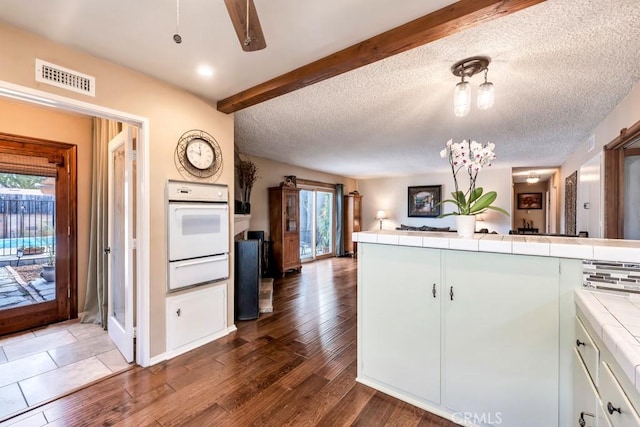 kitchen with white cabinetry, beam ceiling, tile counters, kitchen peninsula, and oven