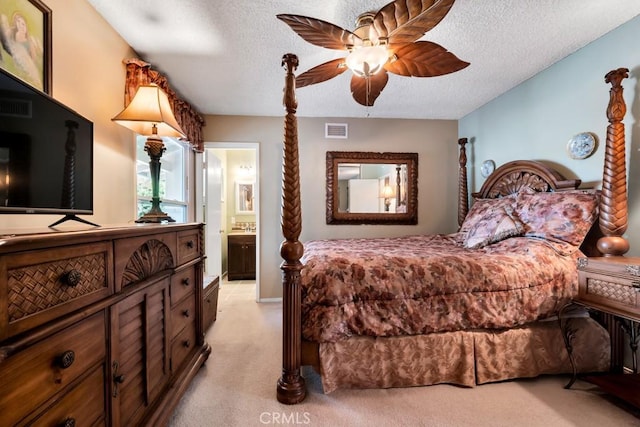 bedroom featuring ceiling fan, ensuite bathroom, light colored carpet, and a textured ceiling