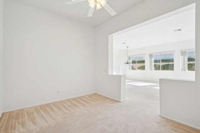 spare room with light carpet and ceiling fan with notable chandelier