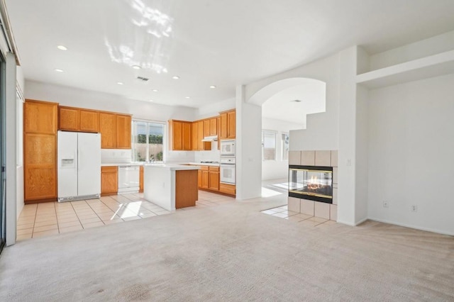 kitchen featuring a tiled fireplace, white appliances, light colored carpet, and a kitchen island