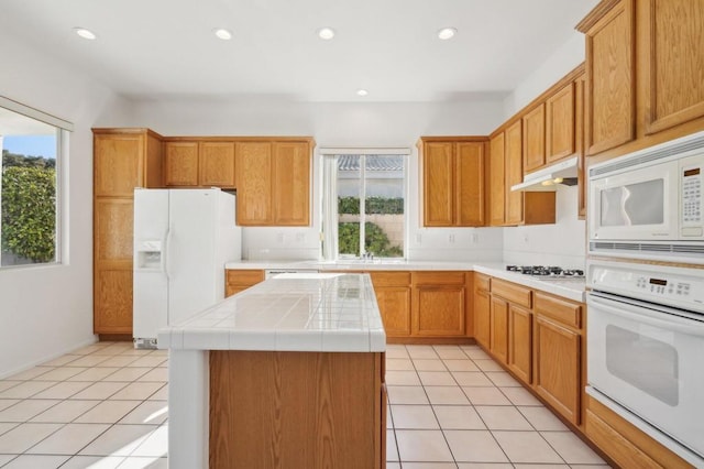 kitchen with a wealth of natural light, a kitchen island, light tile patterned floors, and white appliances