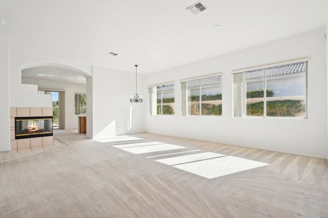 unfurnished living room featuring a tile fireplace, light colored carpet, and a chandelier