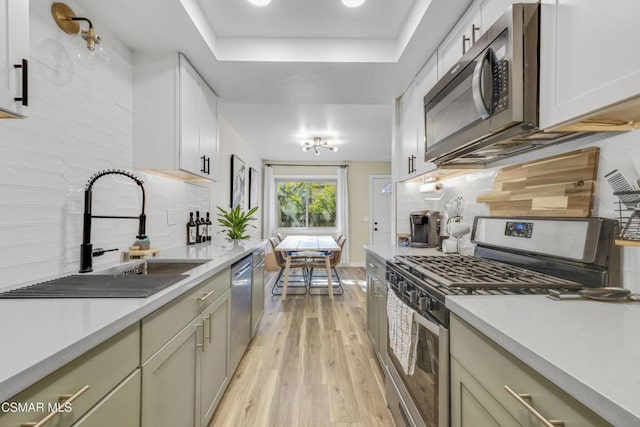 kitchen featuring sink, tasteful backsplash, light wood-type flooring, appliances with stainless steel finishes, and a raised ceiling