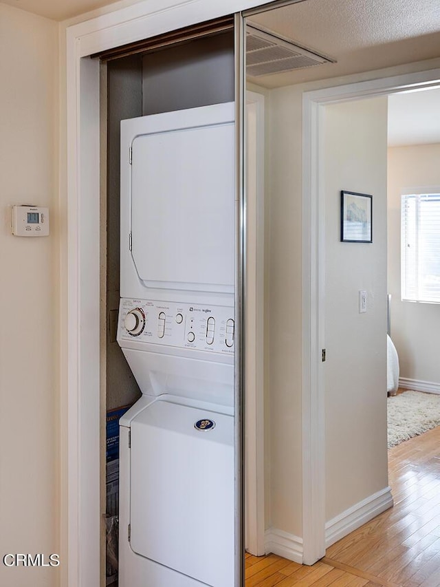 washroom featuring stacked washer / drying machine, a textured ceiling, and light wood-type flooring