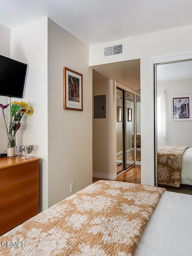 bedroom with electric panel, hardwood / wood-style floors, and a closet