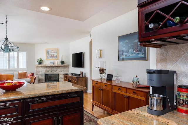 kitchen featuring light stone counters, tasteful backsplash, a brick fireplace, hanging light fixtures, and light hardwood / wood-style floors