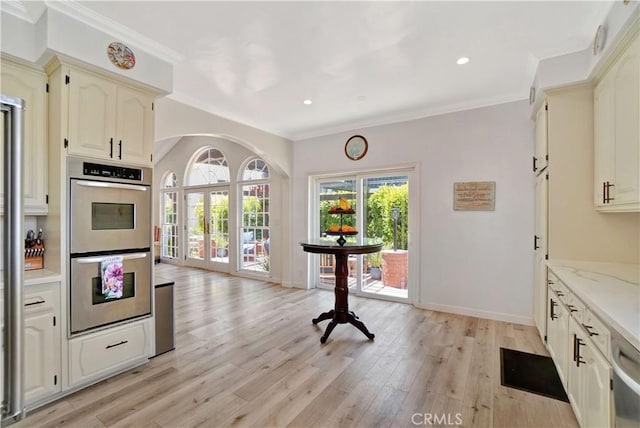 kitchen with ornamental molding, appliances with stainless steel finishes, light stone counters, and light hardwood / wood-style floors