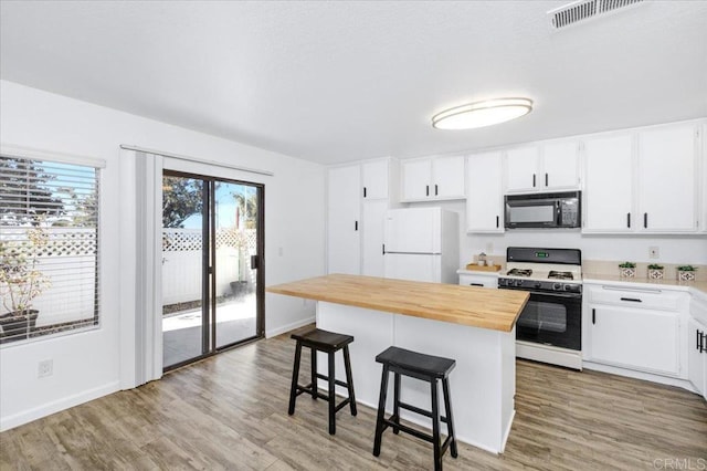 kitchen with black microwave, butcher block counters, a kitchen breakfast bar, freestanding refrigerator, and gas stove