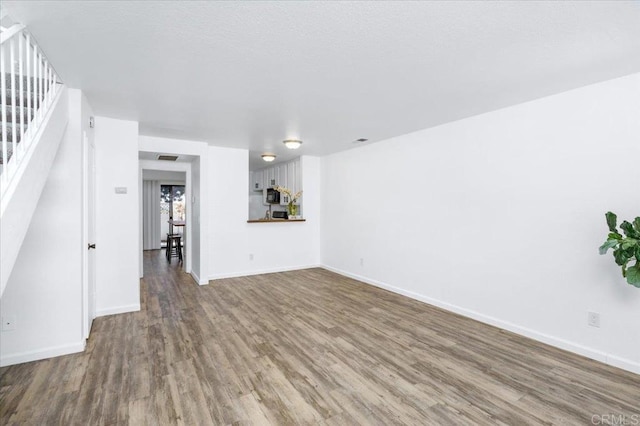 unfurnished living room with stairs, baseboards, and wood finished floors