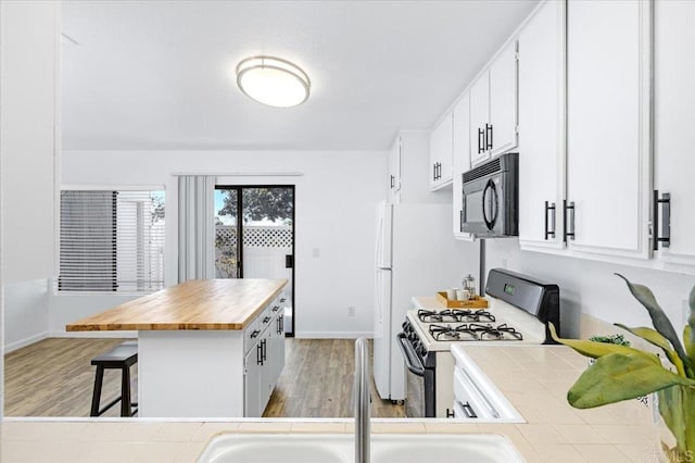 kitchen with range with gas stovetop, light wood-type flooring, a kitchen bar, black microwave, and wooden counters