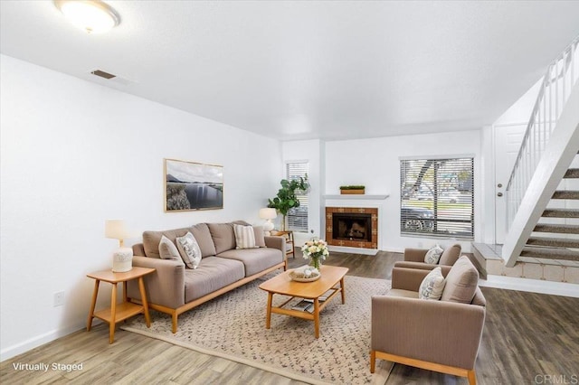 living room with a fireplace, wood finished floors, visible vents, baseboards, and stairway